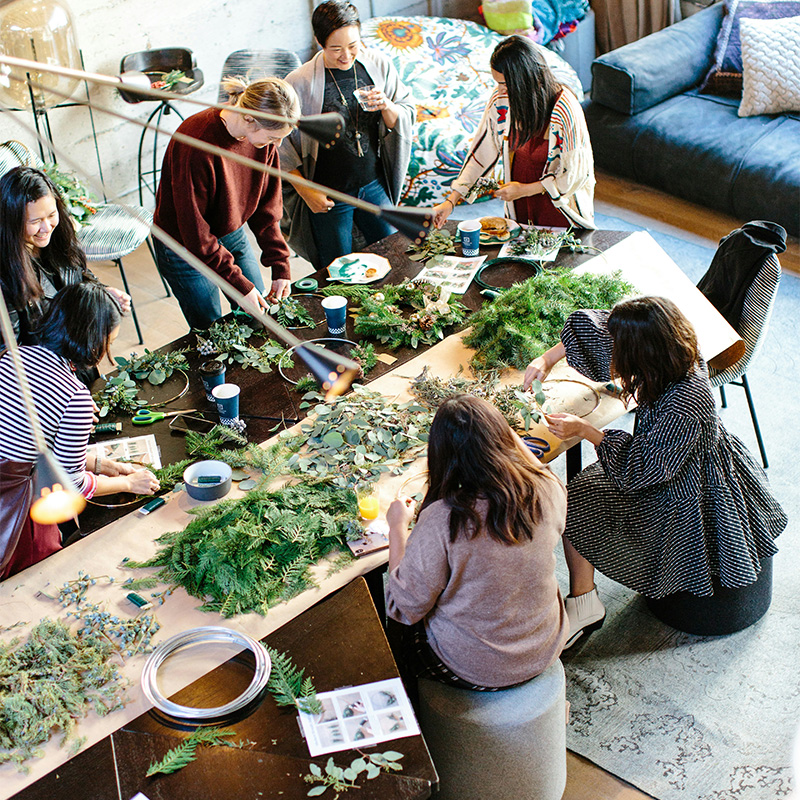 Sju glada personer är samlade runt att stort bord. Bordet är fyyllt med grenar och gröna blad.